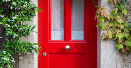 Close up of a red entrance door with jasmine flowers around.