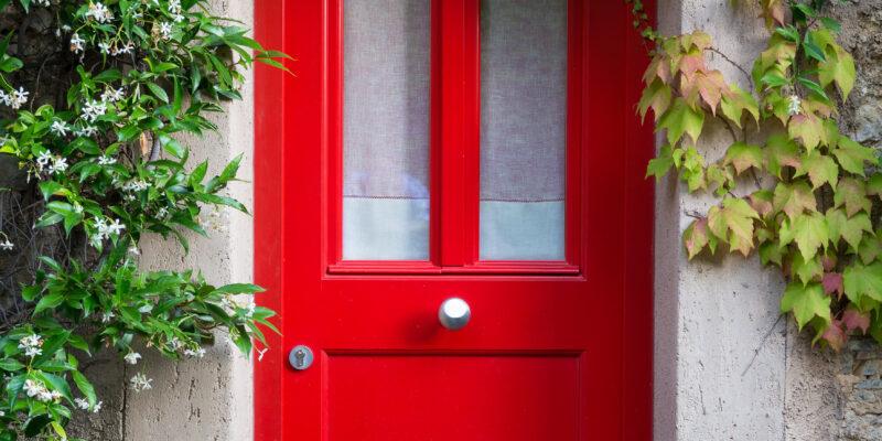 Close up of a red entrance door with jasmine flowers around.