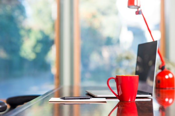 A modern loft space with a desk, laptop, table lamp and red coffee cup.