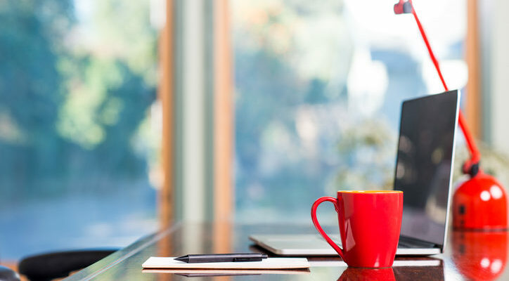 A modern loft space with a desk, laptop, table lamp and red coffee cup.