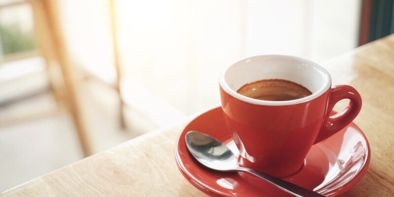 Red cup of espresso on wooden table in coffee cafe. selective focus. Vintage tone.