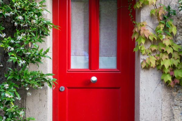 Close up of a red entrance door with jasmine flowers around.