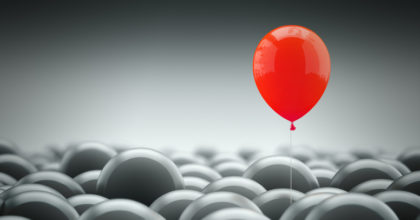 Different, unique and standing out of the crowd concept. A red baloon is different and above the other gray ones, representing the individuality in the masses.