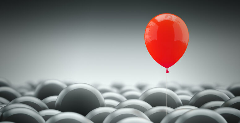 Different, unique and standing out of the crowd concept. A red baloon is different and above the other gray ones, representing the individuality in the masses.