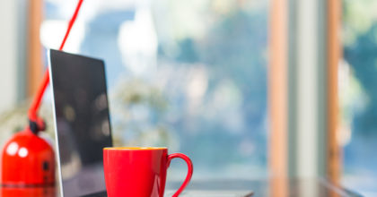 A modern loft space with a desk, laptop, table lamp and red coffee cup.