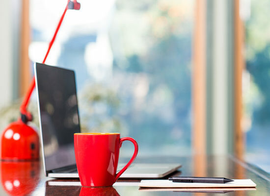 A modern loft space with a desk, laptop, table lamp and red coffee cup.