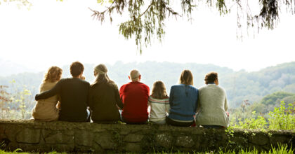 Rear view of multi-generation family relaxing in row on retaining wall against clear sky