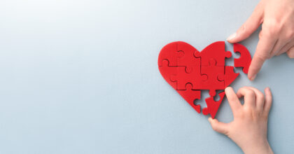 The concept of charity, love, donate and helping hand. International cardiology day. A woman and child arranges red heart shape puzzles. Symbol of helping others.