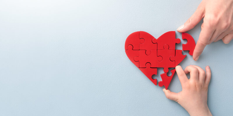 The concept of charity, love, donate and helping hand. International cardiology day. A woman and child arranges red heart shape puzzles. Symbol of helping others.