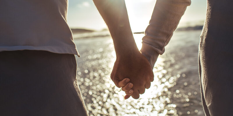 Cropped shot of an older couple holding hands at the beach