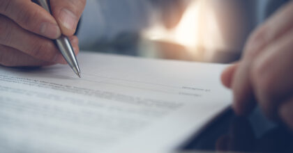 Businessman with pen in hand reading official business contract, rental agreement before making a deal. Man project manager signing document in office, close up.